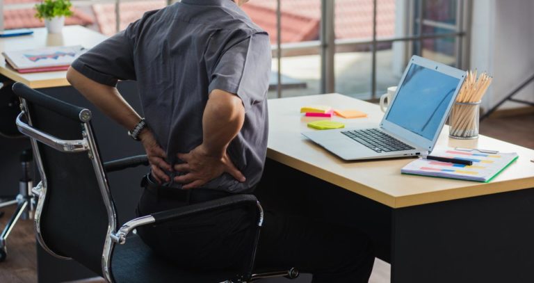 homme qui se tient le bas du dos devant un bureau